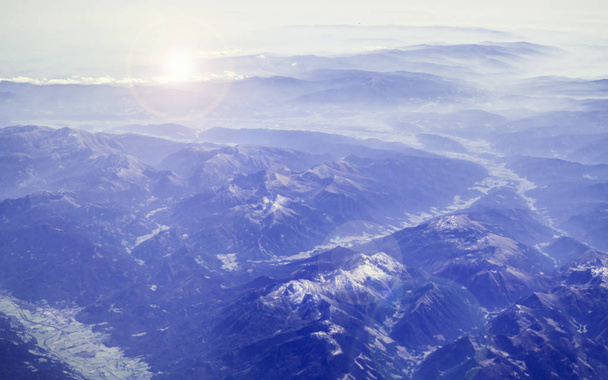 Вид з літака на Альпи. Дивовижний краєвид світанку і гірських вершин у снігу, фіолетовий відтінок і яскраві моменти на фотографії - Фото, зображення