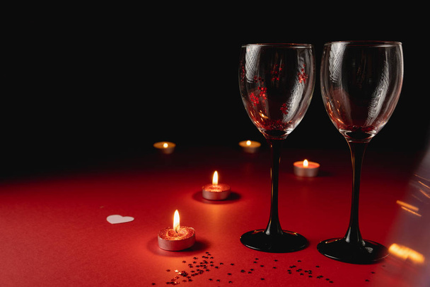 Holiday background. Two clinking wine glasses, candle, confetti on red and black background. Minimal style and valentines day concept. Flat lay, copy space - Fotoğraf, Görsel