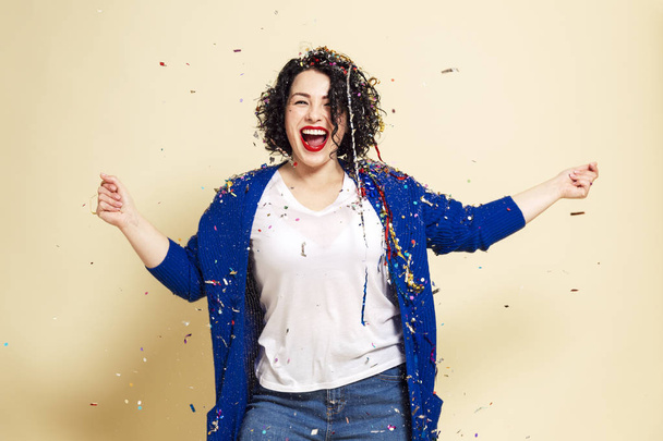 Young laughing woman in confetti celebrates. Yellow background. - Фото, изображение
