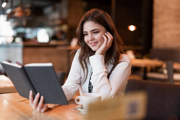 junge schöne Frau in weißer Jacke überprüft ihren Planer, der außerhalb des Büros arbeitet, und trinkt heißen Kaffee im angesagten Café Multitasking moderne Geschäftsfrau - Foto, Bild