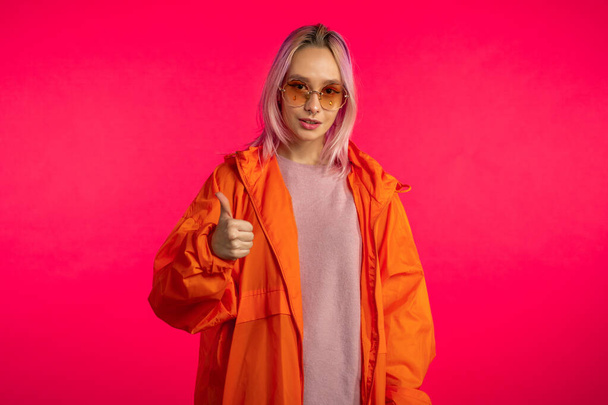 Young hipster making thumbs up sign over pink background. Winner. Success. Positive girl smiles to camera. Body language. - Valokuva, kuva