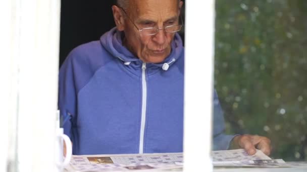 retired man wonders at crossword view through window - Materiał filmowy, wideo