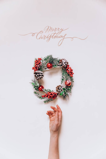 Wreath frame van dennen- en kerstdecor in vrouwelijke handen op een lichte achtergrond. Vlakke lay, elegante stijl. Vrolijk kerstminimalisme beletteren - Foto, afbeelding