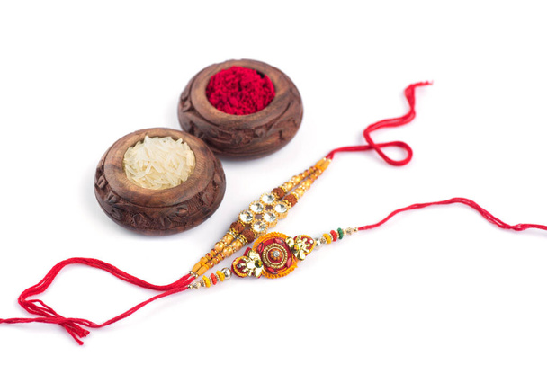 Raksha Bandhan background with an elegant Rakhi, Rice Grains and Kumkum on a white background. A traditional Indian wrist band which is a symbol of love between Brothers and Sisters. - Фото, изображение