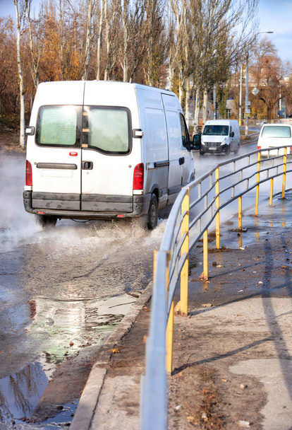 Vrachtwagens rijden langs een weg gevuld met warm water, na het doorbreken van de verwarming van de stad belangrijkste, een metalen hek scheidt de rijbaan van de stoep. - Foto, afbeelding
