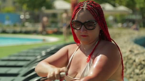 A woman on a deck chair by the pool is smeared with sunscreen. - Imágenes, Vídeo