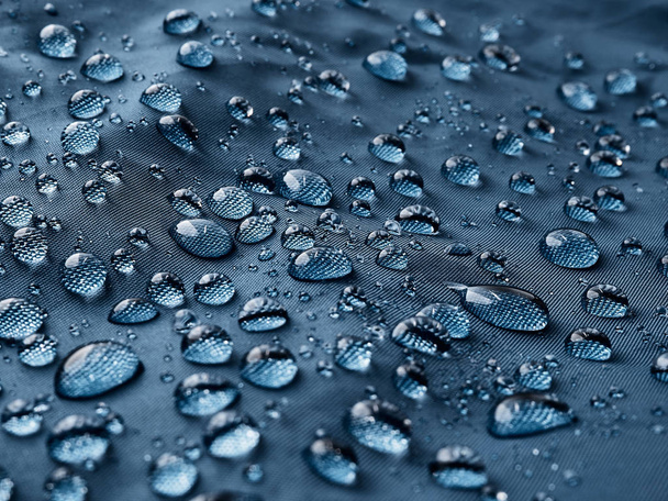 Krople wody deszczowej na niebieskie włókna wodoodporne tkaniny. Niebieskie tło. - Zdjęcie, obraz