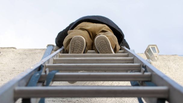 Χαμηλή γωνία θέασης ενός τεχνίτη αναρρίχηση σε μια σκάλα χάλυβα. - Φωτογραφία, εικόνα