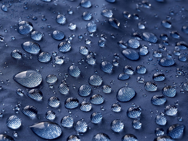 Rain water droplets on blue fiber waterproof fabric. Blue background. - Photo, Image
