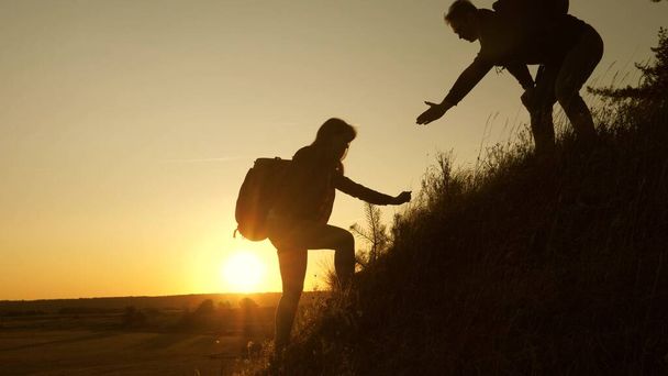 Tourists climb the mountain at sunset, holding hands. teamwork of business people. Traveler man holds out a womans hand to a traveler climbing to the top of the hill. Happy family on vacation. - Photo, Image