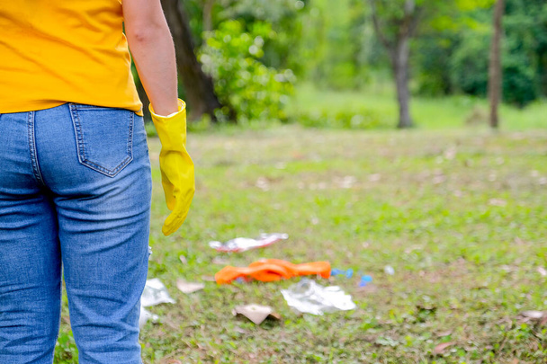 Задняя часть желтой футболки женщина стоять в саду и смотреть, как она поможет очистить мусор
. - Фото, изображение