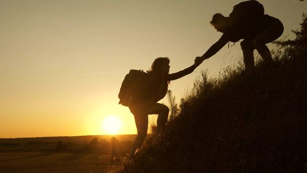 Tourists climb the mountain at sunset, holding hands. teamwork of business people. Traveler man holds out a womans hand to a traveler climbing to the top of the hill. Happy family on vacation. - Photo, Image