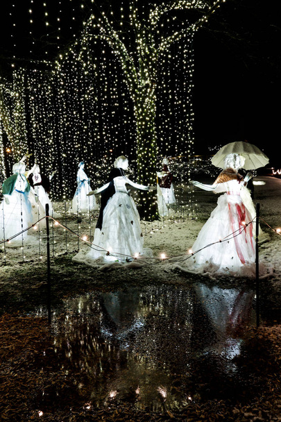 Vrouw figuren dansen in witte jurken onder felle tekenreeks lichten op de sneeuw. Kerst thema installatie. - Foto, afbeelding
