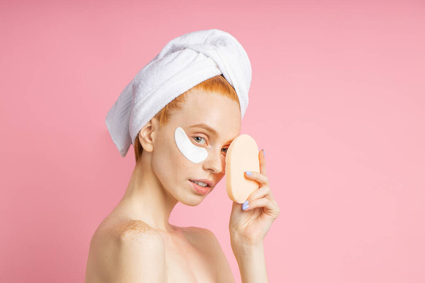 Shot of young woman applies eye patches and holding cosmetic sponge - Fotoğraf, Görsel