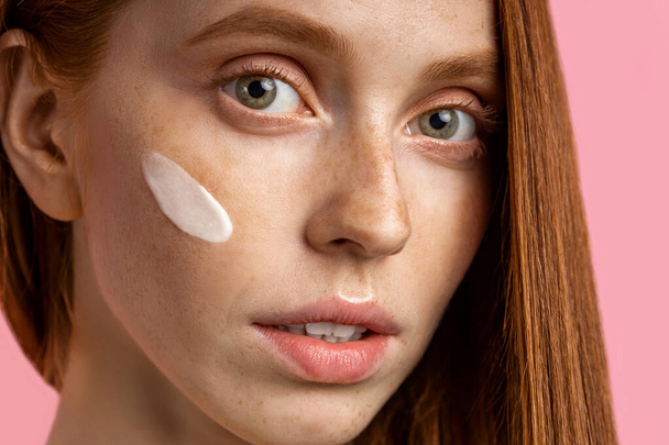 Beautiful young ginger woman with cream on face - Фото, изображение