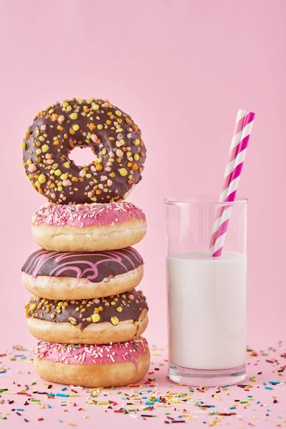 barevné koblihy glazury s posypy a sklenice mléka na růžovém pozadí - Fotografie, Obrázek