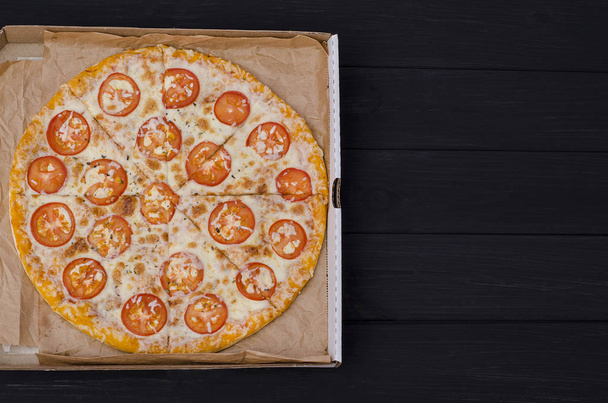 Pizza with cheese and tomatoes in a box with copy space on a dark wooden background. For menus and advertising pizzerias - Photo, Image