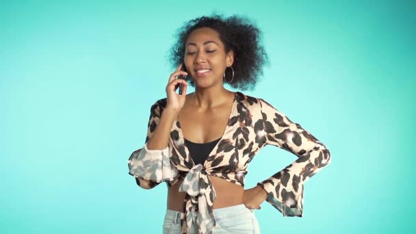 African american woman speaks on phone and smiling from interlocutors jokes. Perfect makeup, trendy outfit. Slow motion. - Materiał filmowy, wideo