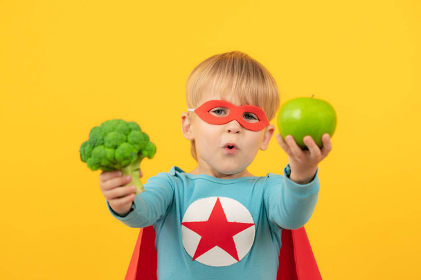 Superhero child holding broccoli and apple - Фото, изображение