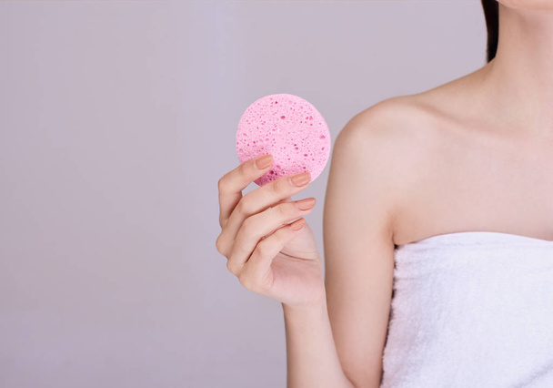 Woman with dark tied hair holds a makeup sponge on her face. - Zdjęcie, obraz