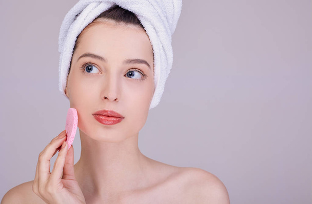 A pensive brunette cleans her face with a sponge. - Foto, Bild