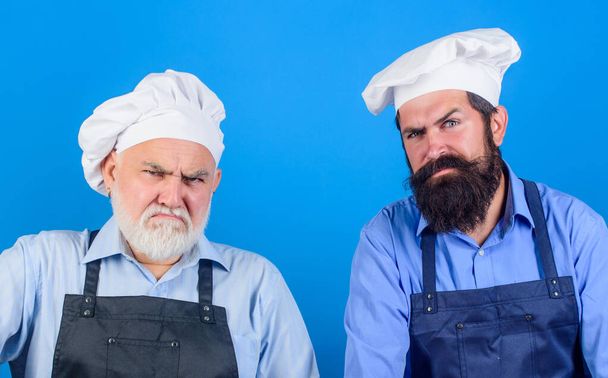 tired of cooking. masters of kitchen. who is the best. father and son cooking together. commercial kitchen at restaurant. professional chefs. serious men in cook hat. mature bearded chef. Our food - Foto, afbeelding