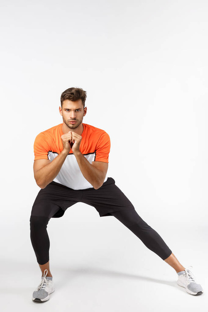Endurance, motivation and fitness concept. Serious-looking focused attractive sportsman perform side squats, clench arms together create tension, workout, gain muscles, white background - Fotoğraf, Görsel