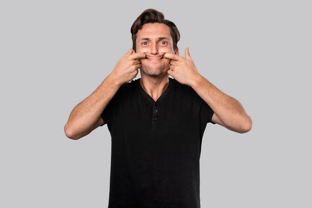 Homem em uma camiseta preta esticando os lábios em um sorriso artificial
. - Foto, Imagem