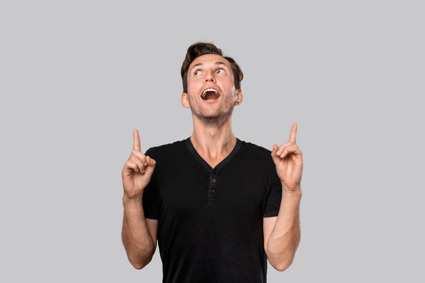 Усміхнений чоловік у чорній трійниковій сорочці вказує пальцем вгору. Копіювати місце для реклами
 - Фото, зображення