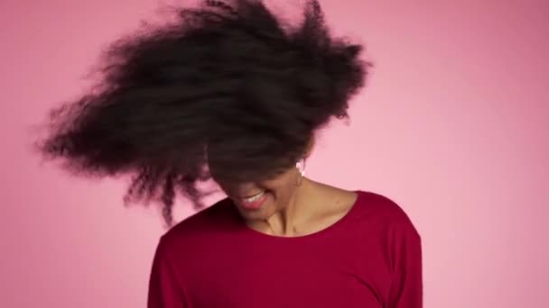 Beautiful african american woman with afro hair having fun smiling and dancing in studio against pink background. slow motion - Materiaali, video