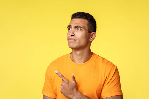 Skeptical, unimpressed serious-looking male student making choice, employee picking workplace, frowning disapproval and dislike, looking pointing upper left corner disappointed, yellow background - Photo, Image