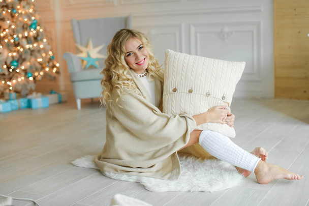 Une jeune femme blonde enveloppée dans une couverture chaude sur le fond d'un sapin de Noël
 - Photo, image