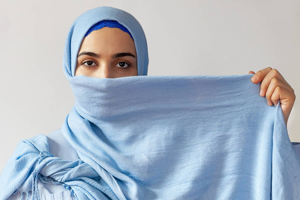 Piękna muzułmanka zakrywa twarz jasnoniebieską szmatką. Islamski styl mody - Zdjęcie, obraz