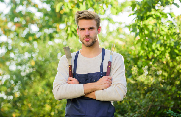 Picnic concept. Bbq chef. Handsome guy cooking food. Grilling food. Barbecue utensils. Cooking burgers. Man hold barbeque equipment. Summer weekend. Tools for roasting meat outdoors. Barbeque party - Foto, afbeelding