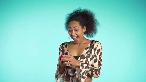 Pretty african-american young woman in leopard print top holding small jewelry box on blue wall background. Girl smiling, she is happy to get present, offer of marriage. - Πλάνα, βίντεο