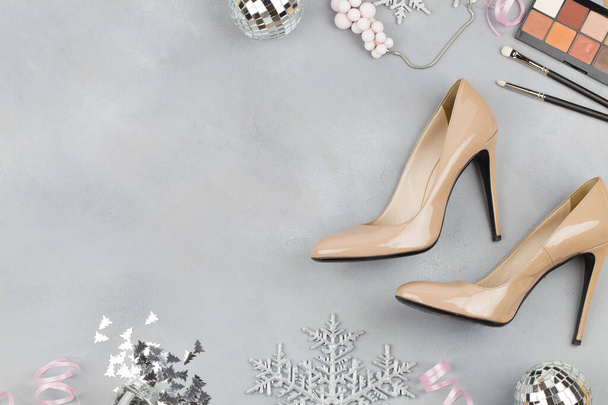 Flat lay beige high heel shoes with christmas decoration, cosmetics and necklace on blue background - Foto, Imagem