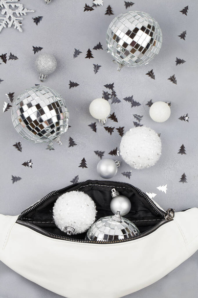 Χριστουγεννιάτικες γιορτινές διακοσμητικές άσπρες και ασημένιες μπάλες και νιφάδες χιονιού που ρέουν από την τσάντα μέσης σε μπλε φόντο - Φωτογραφία, εικόνα
