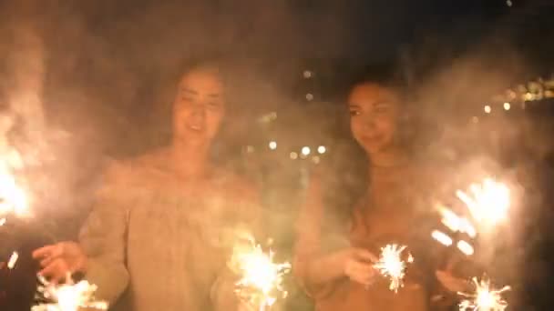 Ünnepi ötlet. Ázsiai lányok játszanak szórakoztató tűzijátékot a parton. 4k felbontás. - Felvétel, videó