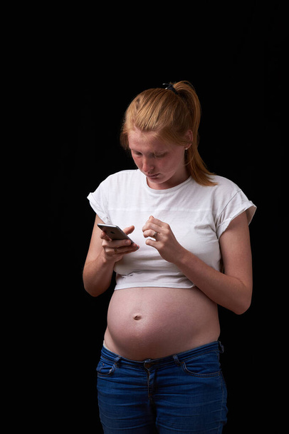 Schwangerschaft, Mutterschaft, Technologie, Menschen und Erwartungskonzept - traurige Schwangere, die zu Hause das Smartphone anruft. Verärgerte Schwangere mit Handy in der Hand. Technologie und Schwangerschaft - Foto, Bild