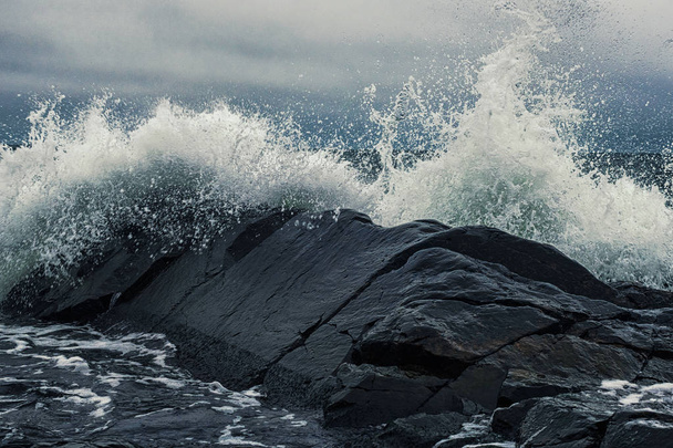 黒い岩の海岸で波が砕ける - 写真・画像