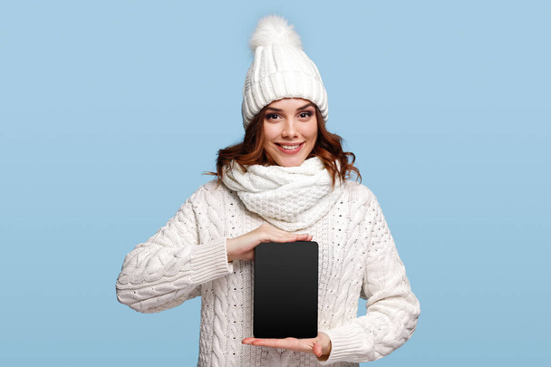 Smiling woman in knitwear holding black blank tablet - Foto, imagen
