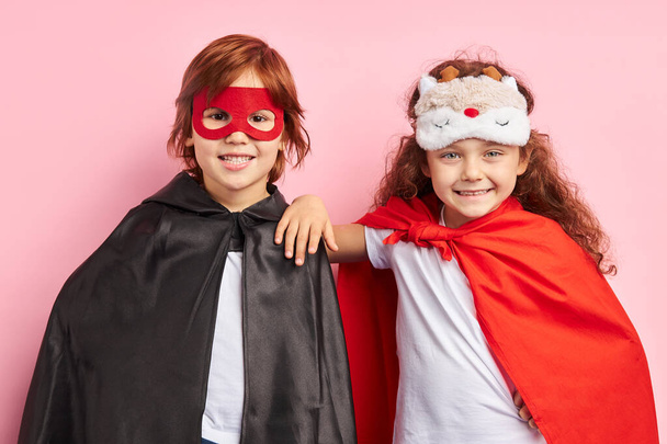 Two smiling kids in superhero suit stand isolated over pink background - Foto, Imagen