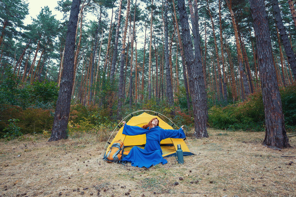 Young girl in blue robe stretching hands, doing exercises in forest camping - Zdjęcie, obraz