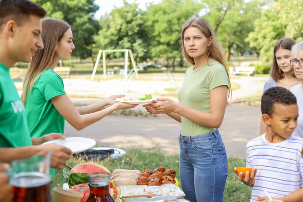 Junge Freiwillige verteilen Lebensmittel an arme Menschen im Freien - Foto, Bild