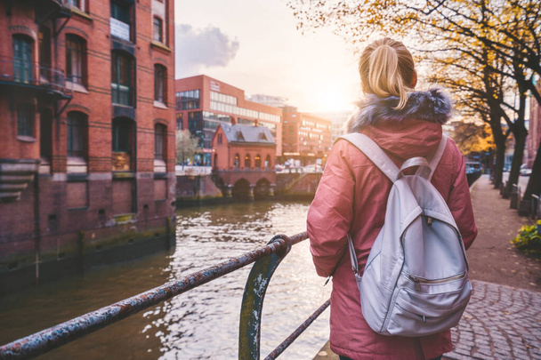 Back rear view of adult woman tourist with backpack enjoying autumn beautiful sunset scene on the Speicherstadt historic warehouse district in Hamburg, Germany, Europe - Photo, image