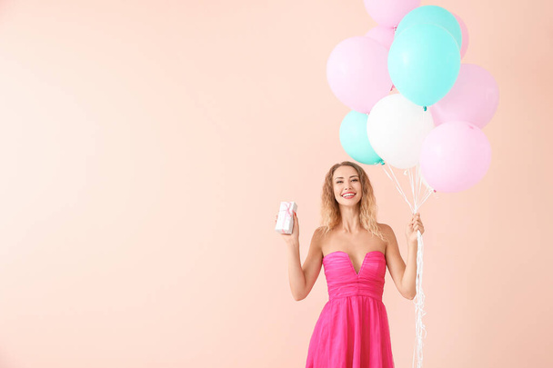 Красива молода жінка з повітряними кулями і подарунком на кольоровому фоні
 - Фото, зображення