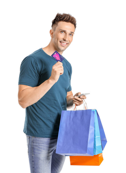 Kredi kartı, alışveriş torbaları ve beyaz arka planda cep telefonu olan genç bir adam. - Fotoğraf, Görsel