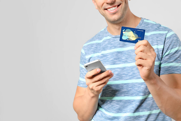 Молодий чоловік з кредитною карткою і мобільним телефоном на світлому фоні
 - Фото, зображення