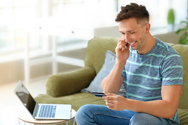 Nuori mies, jolla on luottokortti, puhuu kotona matkapuhelimella
 - Valokuva, kuva