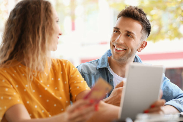 Молодая пара с кредитной картой и планшетным компьютером сидит в кафе
 - Фото, изображение